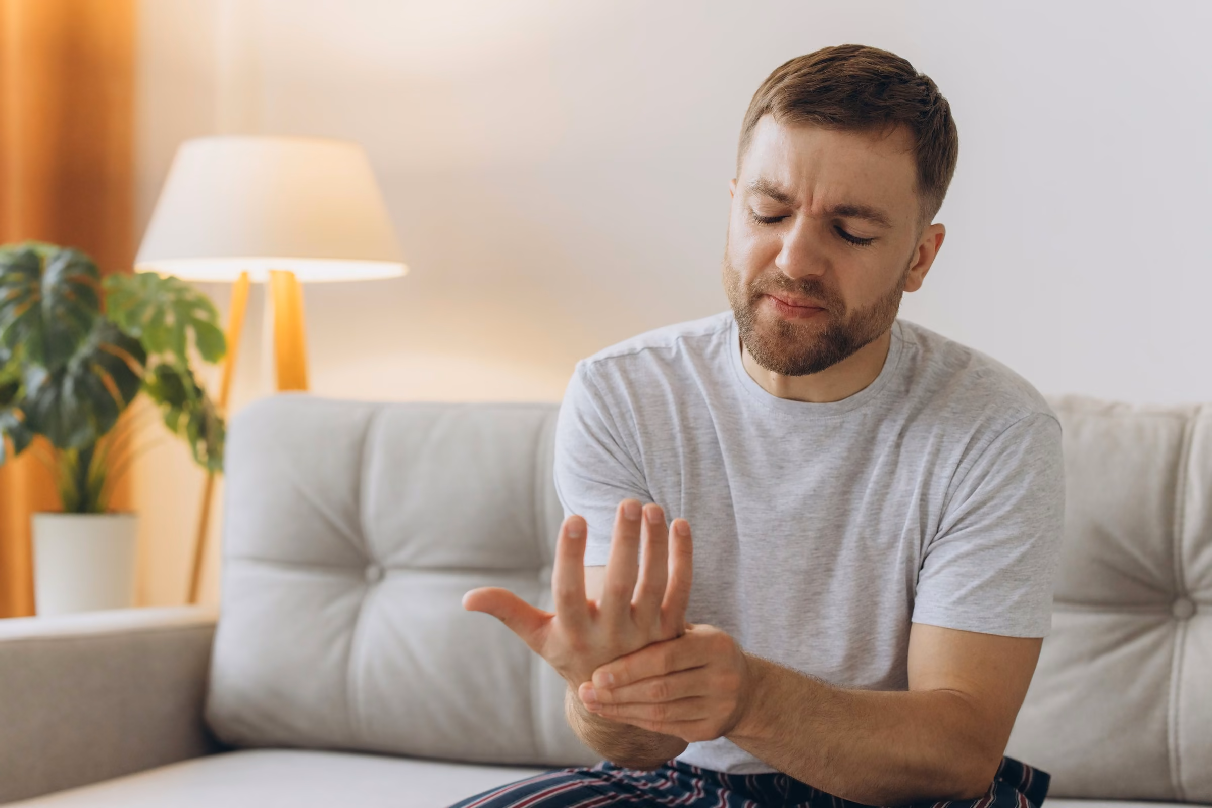 Mann sitzt abends auf dem Sofa und hält sich das schmerzende Handgelenk