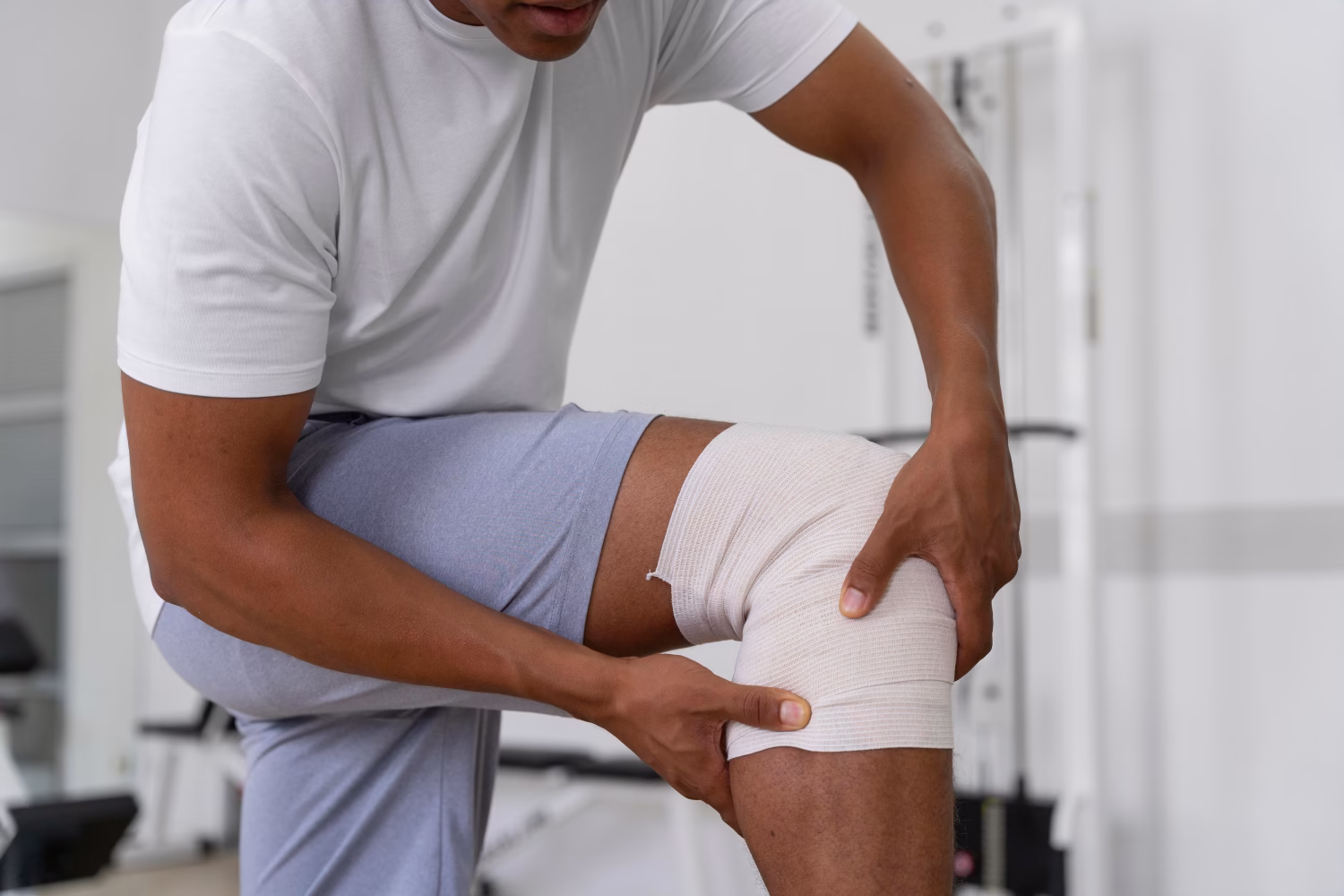 Nachsorge nach einer Kniearthroskopie Physiotherapeut stützt das bandagierte Knie eines Patienten bei einer Übung.